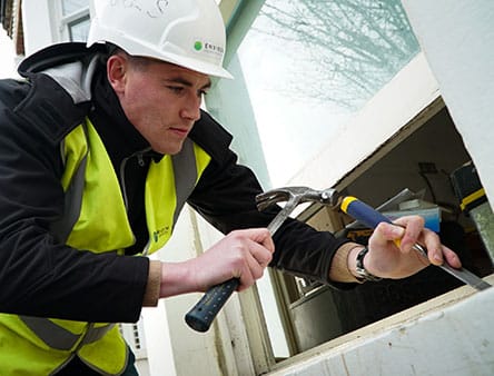 Man in hard hat and high-visibility vest repairing a window, demonstrating restoration services for period homes.