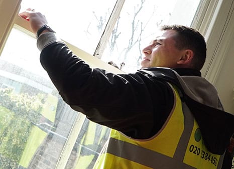Man in a high-visibility vest restoring sash windows in a listed building, highlighting the importance of heritage property preservation and compliance with restoration standards.