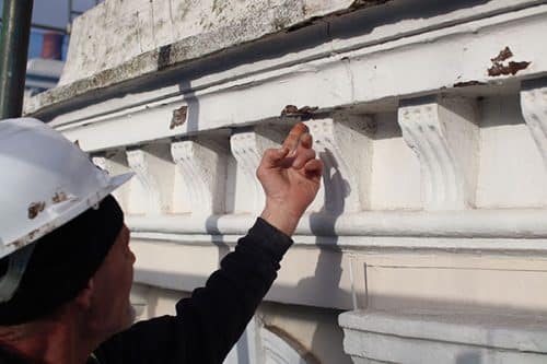 Worker inspecting decorative architectural details during renovation of Rhydoldog House, highlighting the challenges of large-scale restoration projects.