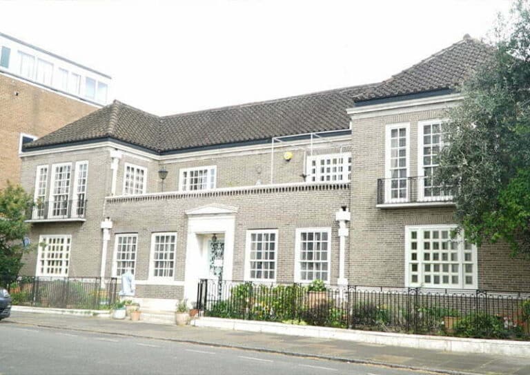 Exterior view of a London property, showcasing a brick building with multiple windows, a central entrance, and a landscaped front area, relevant to expert damp survey services.