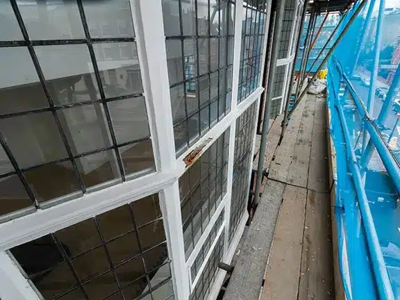 Timber sash windows undergoing restoration on a scaffolded building, highlighting the preservation of historical architecture in London.