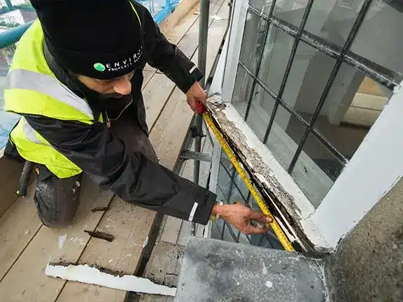 Worker measuring and repairing window frame during restoration of historic building, showcasing Environ Restoration Services' expertise in preserving architectural heritage.