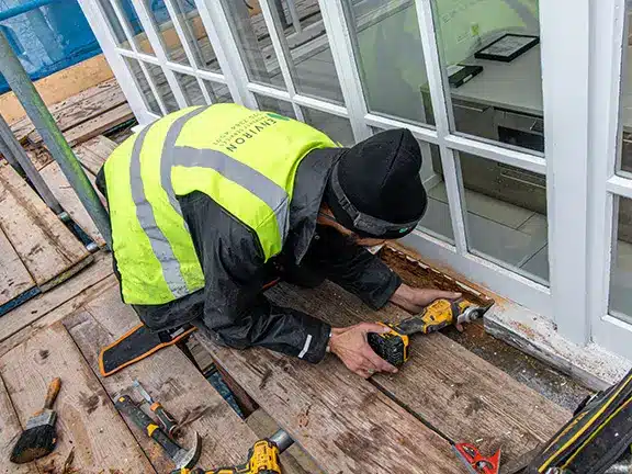 Worker in safety gear repairing window frame during restoration project, surrounded by tools on a wooden platform, emphasizing Environ Restoration's commitment to preserving historic architecture in London.
