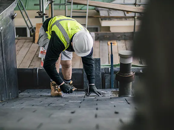 Worker in safety gear repairing a historic roof, focusing on craftsmanship and preservation of period building architecture.