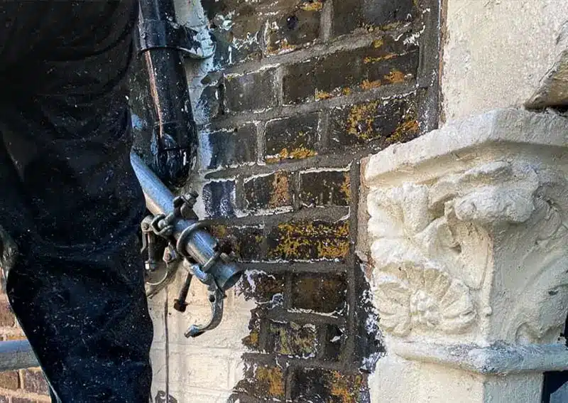 Worker applying damp proofing treatment to brick wall, addressing moisture issues and mould prevention, with ornate stonework visible.