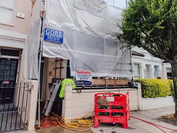 Scaffolded communal property undergoing restoration with signage indicating contractor details and a warning notice, reflecting Section 20 works in London.