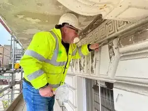 Professional contractor inspecting heritage building restoration, wearing safety gear and working on decorative moulding.