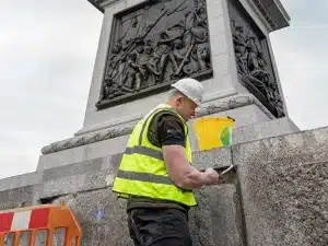 Worker in high-visibility vest applying cleaning solution to stone masonry, showcasing professional restoration techniques for heritage buildings.