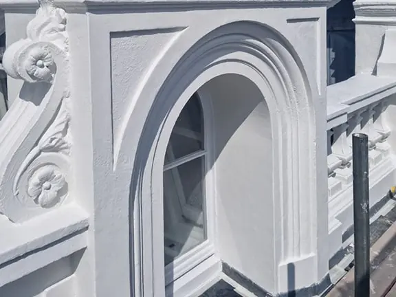 Detailed architectural restoration of a listed building featuring ornate white plasterwork, an arched window, and decorative elements, showcasing Environ Restoration Services' expertise in maintaining historic properties.