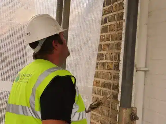Construction worker in high-visibility vest and hard hat inspecting brick wall during restoration project at a heritage building.