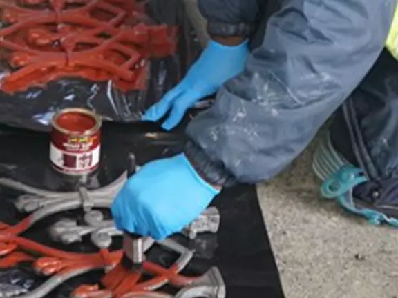 Person applying red paint to metal restoration elements, wearing blue gloves, showcasing skilled craftsmanship in building refurbishment.