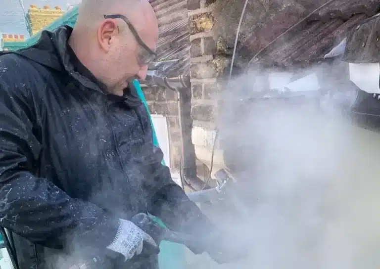 Man using steam cleaning equipment for property restoration, surrounded by historic building materials, emphasizing period property conservation techniques.
