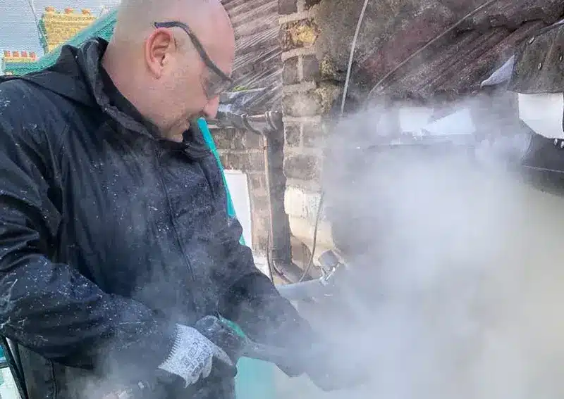 Professional using ThermaTech technology for brick paint removal, surrounded by steam and debris, demonstrating effective restoration techniques.