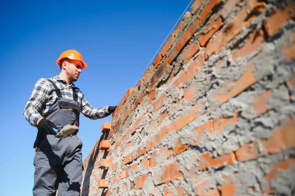 Construction worker in safety gear applying mortar to brick wall, highlighting restoration techniques relevant to repointing and building preservation.