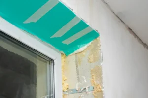Interior wall preparation with masking tape applied, showing exposed insulation and unfinished surface, relevant to restoration and renovation projects.