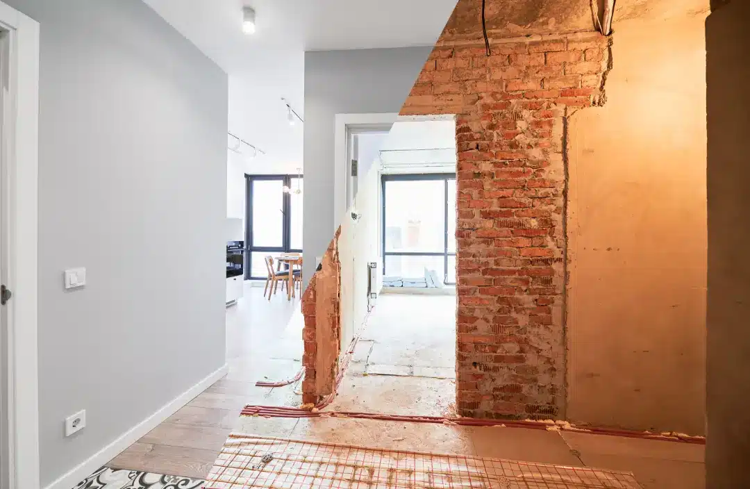 Interior space showcasing a contrasting renovation and restoration process, featuring exposed brick wall on one side and modern, finished space on the other, illustrating key differences in home improvement approaches.