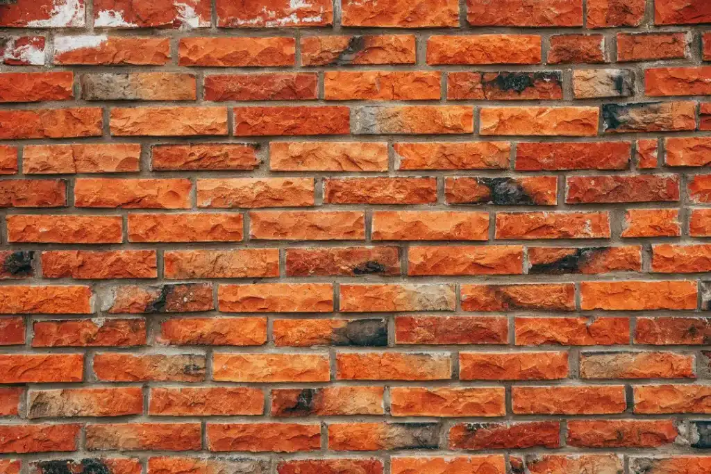 Close-up of a textured brick wall showcasing various shades of orange and brown, highlighting potential cleaning issues and maintenance considerations for brick surfaces.