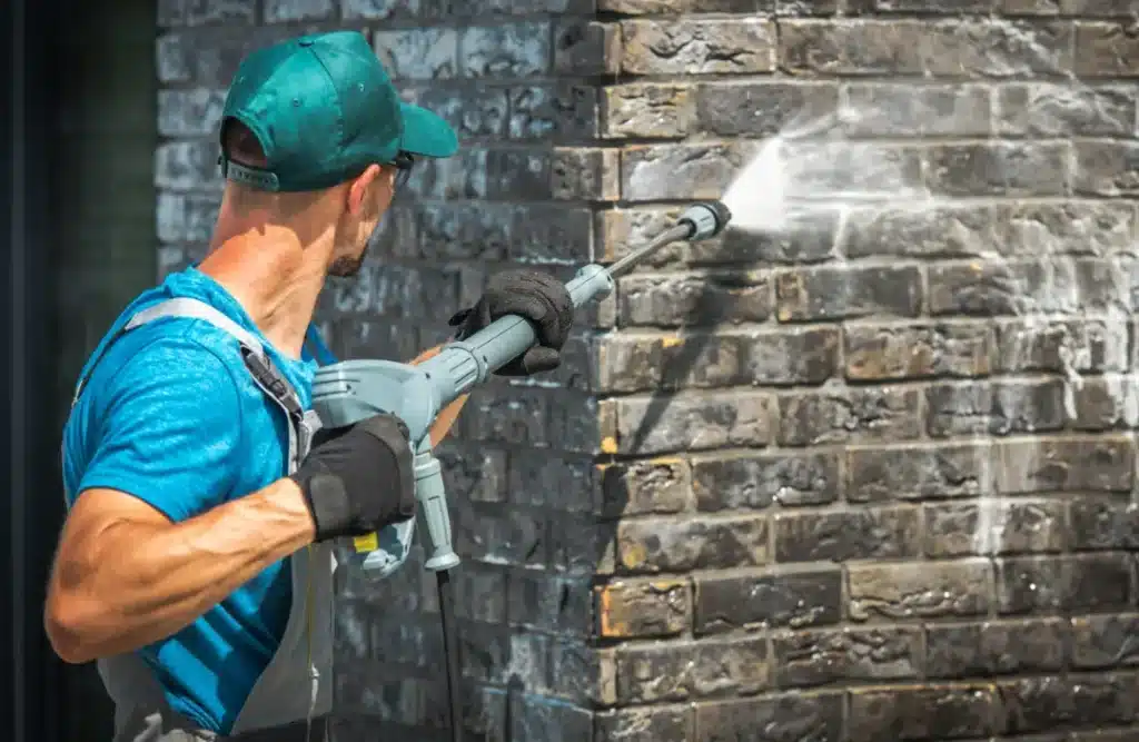 Professional cleaner using a pressure washer on a brick wall, illustrating the process of expert brick cleaning to enhance aesthetic appeal and maintain structural integrity.