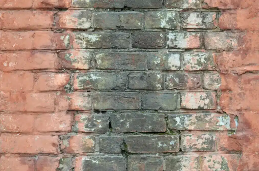 Brick wall showing weathered and discoloured sections, highlighting challenges in masonry repairs during winter due to cold temperatures and potential damage to mortar.