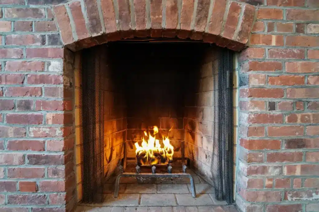 Brick fireplace with flames burning in the grate, showcasing a clean and well-maintained interior, illustrating effective fireplace cleaning methods.