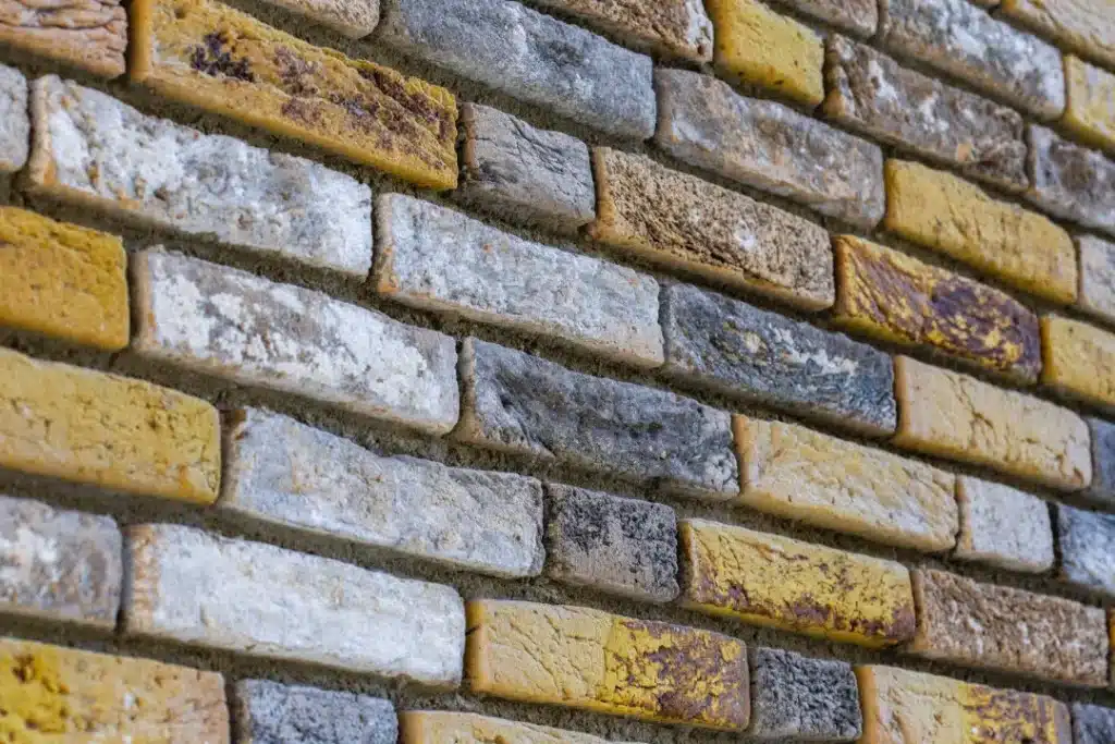 Textured brick wall featuring varying shades of grey, yellow, and white, illustrating the importance of masonry quality and seasonal considerations for brickwork repairs.