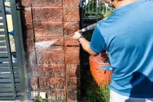 Person using a pressure washer to clean brick wall, demonstrating effective brick cleaning techniques for restoration services.