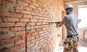 Worker using a drill on a brick wall, demonstrating restoration techniques for brick cleaning and maintenance.