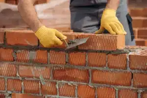 Person in yellow gloves laying bricks with trowel, illustrating brickwork restoration techniques relevant to maintaining and cleaning brick structures.