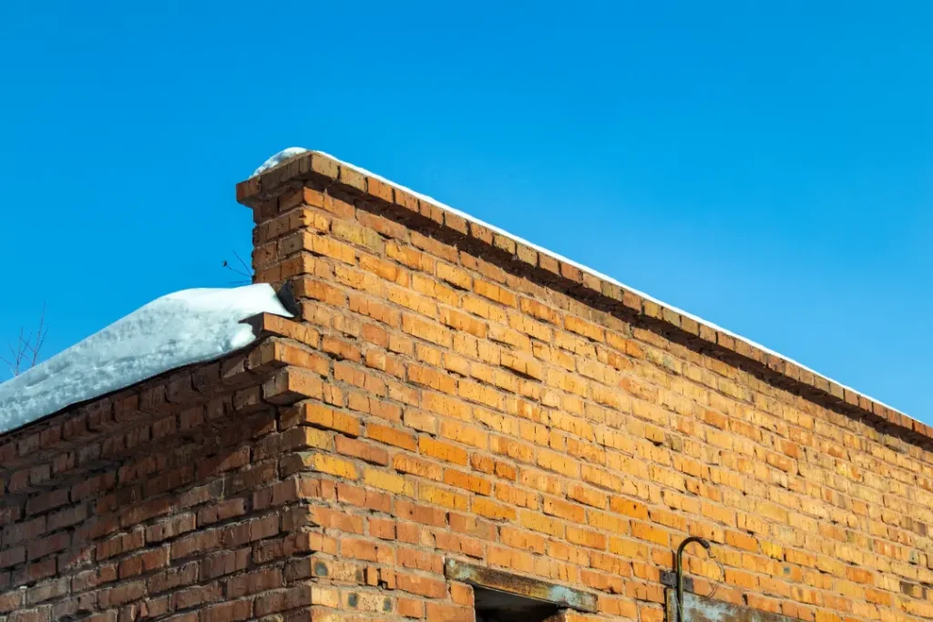 Brick wall with snow on top, clear blue sky, illustrating winter conditions affecting masonry and highlighting potential freeze-thaw damage risks.
