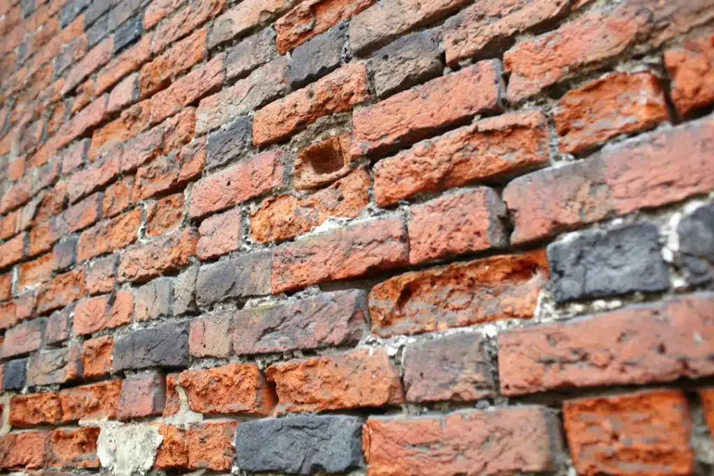Close-up of weathered brick wall displaying various shades of red and black bricks, highlighting surface texture and potential areas for restoration, relevant to discussions on brick cleaning and pebbledash removal.