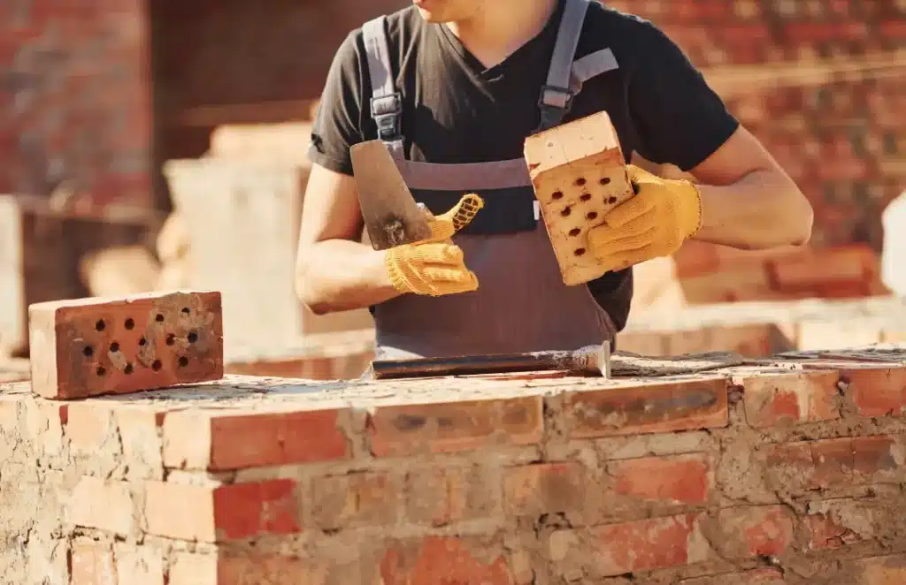 Worker preparing bricks for cleaning, holding two bricks and a trowel, with focus on proper preparation techniques for brick restoration.