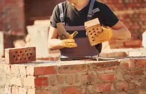 Person in gloves holding bricks, assessing brick quality for restoration, with brickwork background, relevant to DIY brick maintenance and cleaning tips.